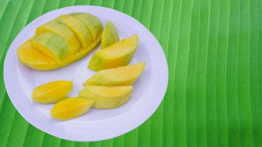Yeşil muz yapraklarının üzerine konmuş beyaz bir tabakta olgun mango dilimleri. Meyveler vitaminlerde yüksektir, sağlık için iyidir..