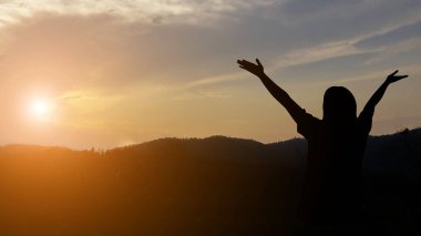 Özgürlükle dolu bir dünyada gün batımında kollarını açan bir kadın doğanın tadını çıkarır..