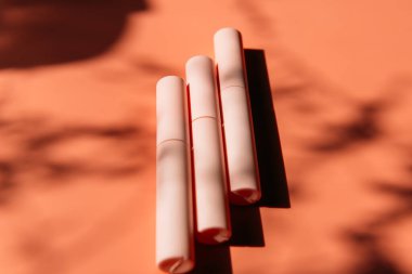 Pembe kapalı maskara tüpleri, göz kalemi, dudak parlatıcısı, şeftali arka planda sıvı ruj gölgeli, kopyalama alanı.