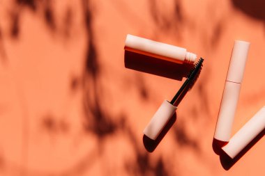 Maskara için pembe temiz makyaj fırçası açık bir tüp, kapalı kozmetik tüpleri, dudak parlatıcısı, sıvı ruj, gölgeli pembe göz kalemi yanında yatar. Boşluğu kopyala