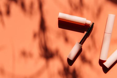 Maskara için pembe temiz makyaj fırçası açık bir tüp, kapalı kozmetik tüpleri, dudak parlatıcısı, sıvı ruj, gölgeli pembe göz kalemi yanında yatar. Boşluğu kopyala