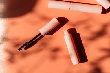 Maskara için pembe temiz makyaj fırçası açık bir tüp, kapalı kozmetik tüpleri, dudak parlatıcısı, sıvı ruj, gölgeli pembe göz kalemi yanında yatar. Boşluğu kopyala