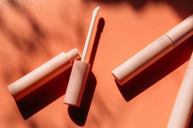 Dudak parlatıcısı için pembe temiz makyaj fırçası, açık bir tüpün yanında sıvı ruj, kapalı kozmetik tüpleri, maskara, gölgeli pembe göz kalemi. Boşluğu kopyala