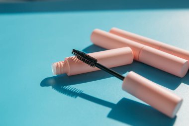 Maskara için pembe temiz makyaj fırçası açık bir tüp, kapalı kozmetik tüpleri, dudak parlatıcısı, sıvı ruj, gölgeli pembe göz kalemi yanında yatar. Boşluğu kopyala