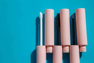 pink tubes of cosmetics and brushes lie on a blue background. Copy space. Closed tubes of lipstick, liquid lip gloss, mascara, eyeliner