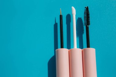 pink brushes for cosmetics, mascara, liquid lipstick, eyeliner, lip gloss on a blue background, copy space