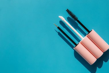 pink brushes for cosmetics, mascara, liquid lipstick, eyeliner, lip gloss on a blue background, copy space