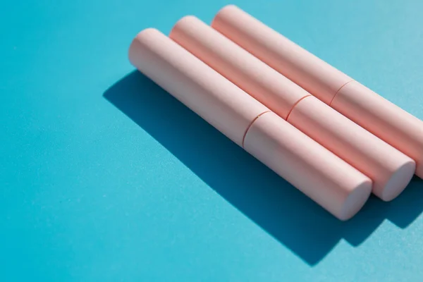 pink tubes of cosmetics on a blue background. Copy space. Closed tubes of lipstick, liquid lip gloss, mascara, eyeliner