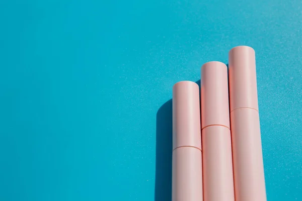 pink tubes of cosmetics on a blue background. Copy space. Closed tubes of lipstick, liquid lip gloss, mascara, eyeliner