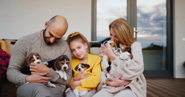 Mutlu bir aile evlerinin kapısında oturup yavru köpeklerle oynuyor. Anne baba ve kızları. — Stok video