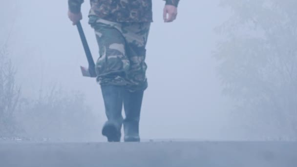 Un uomo con un'ascia cammina lungo la strada nella nebbia - una scena terribile — Video Stock