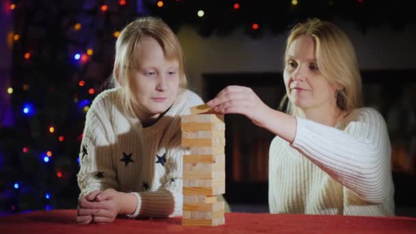 Meisje met mam spelen een bordspel op de achtergrond van wazige lichten van feestelijke slingers — Stockvideo