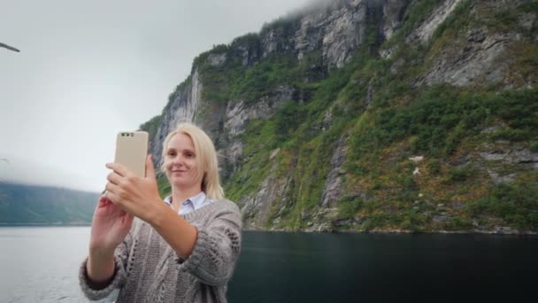 Una mujer toma fotos de sí misma en el contexto del fiordo noruego. Viajar en un crucero — Vídeo de stock