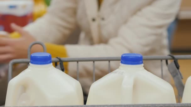 El cliente descarga las compras del carrito y las coloca en la cinta en la caja registradora. Grandes botellas de leche en primer plano — Vídeos de Stock