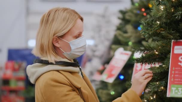 보호용 마스크를 쓰고 있는 여성 이 가게에서 크리스마스 트리를 고르고 있다. 겨울철 휴일 의안 전 한 쇼핑 — 비디오