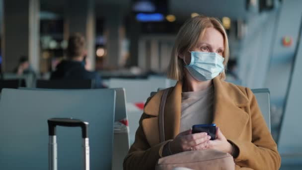 Egy védőmaszkos nő portréja, aki a reptér terminálján ül, és a repülésre vár. — Stock videók