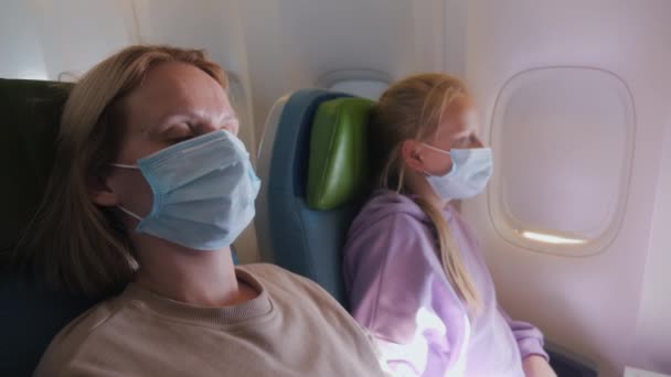 Egy nő egy gyerekkel, aki repülőn repül, védőmaszkot visel. Belefáradtam a tegel repülésbe. — Stock videók