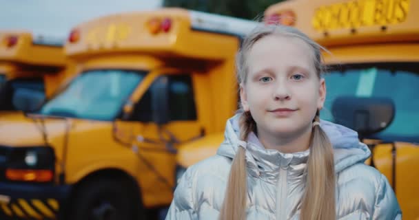 Portrait d'une écolière sur fond d'autobus scolaires jaunes — Video