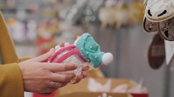 O comprador tem um boneco de neve de brinquedo em suas mãos escolhe decorações para a árvore de Natal — Vídeo de Stock