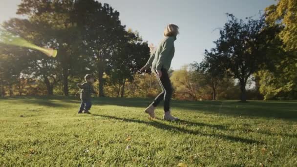 Una donna si diverte con il suo bambino, correndo insieme sull'erba sotto i raggi del sole — Video Stock