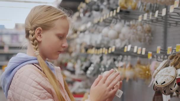 El niño elige decoraciones para el árbol de Navidad, se para en la vitrina con juguetes en la tienda — Vídeos de Stock