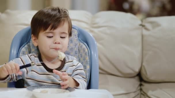 Ein cooler kleiner Junge isst selbstständig Knödel. Sitzt im Hochstuhl — Stockvideo