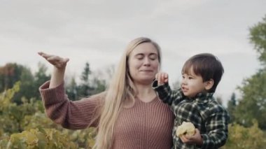 Mutlu anne, kollarında elma yiyen Asyalı bir bebek tutuyor.