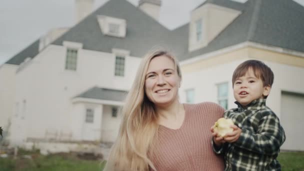 Retrato de una madre feliz con un bebé en sus brazos sobre el fondo de una casa grande — Vídeos de Stock