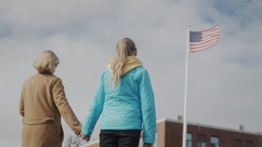 Anne ve çocuk el ele tutuşup ofis binasının önündeki Amerikan bayrağına bakıyorlar.