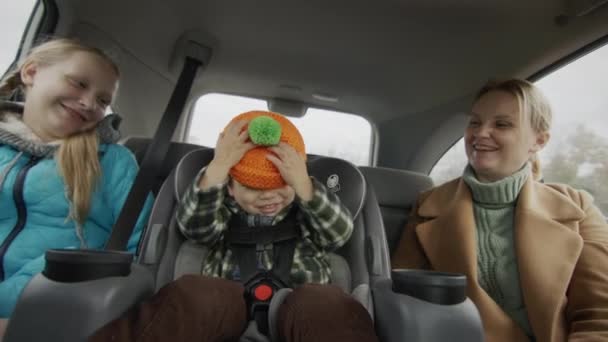 Une famille joyeuse monte sur le siège arrière d'une voiture - une mère, un petit enfant avec une fille de dix ans. Amuse-toi. — Video