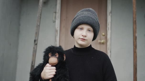 Portrét smutné dívky, stojící na prahu domu, držící v rukou opičku — Stock video