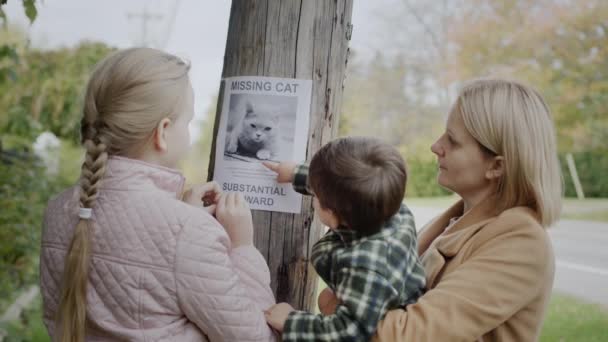 A woman with two children attaches a leaflet about a missing cat to a pole — Stock Video