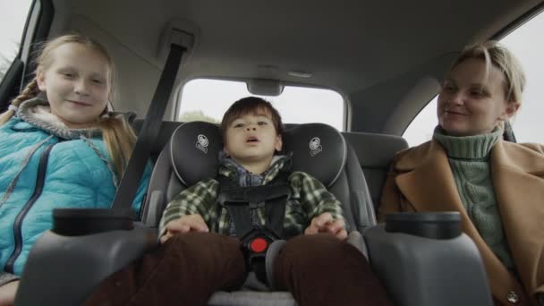 A companhia alegre despreocupada monta no assento traseiro do carro. Mãe com dois filhos — Vídeo de Stock