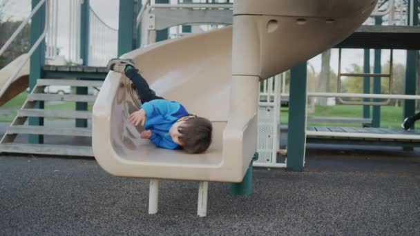 Ein kleiner Junge schlägt beim Abstieg von einer Kinderrutsche mit dem Kopf auf. Verletzungen bei Kindern. — Stockvideo