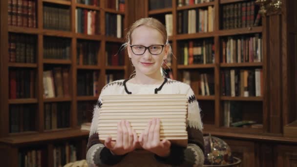 손에 교과서가 쌓여 있는 여대생의 모습은 도서관에 있는 책들이 뒤엉켜 있는 선반을 배경으로 서 있다. — 비디오