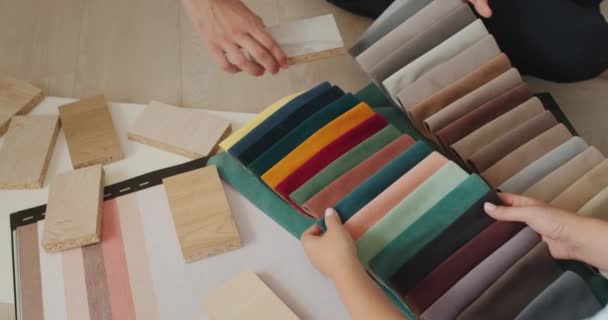 Top view: Two spouses choose a finish for their home, look at samples of wood, fabric and wallpaper. Close-up shot — Stock videók