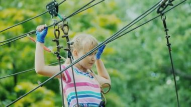 The child has fun in the rope town - climbs high above the ground in the branches of trees
