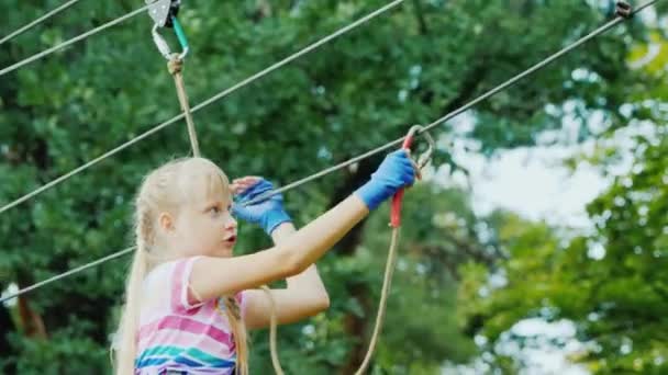 The child uses insurance ropes, climbs the ropes among the tall trees — Vídeo de Stock