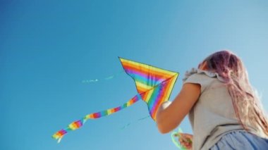 Low angle video - Girl plays with kite that flies high in blue sky