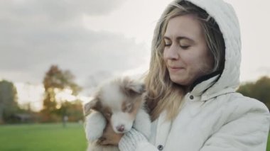 Genç bir kadın elinde şirin bir köpek yavrusu tutuyor, yavru köpek yüzünü yalıyor. Sonbahar parkında birlikte yürüyoruz..