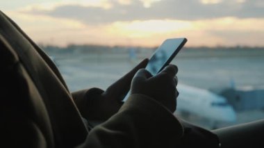 Akıllı telefonlu yolcu elleri. Arka planda, bir pencere ve uçaklar