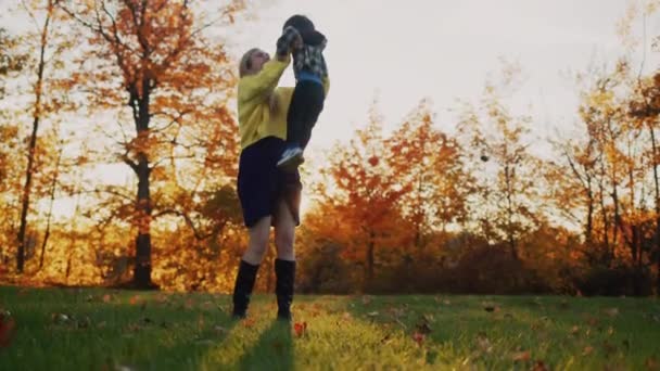 En ung mor leker med sin unge son - spyr upp honom. Ha det så trevligt på en promenad i parken — Stockvideo