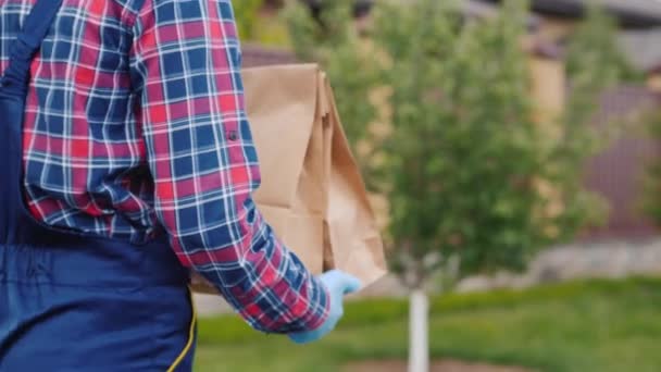 Πίσω όψη: Ένας υπάλληλος της υπηρεσίας παράδοσης μεταφέρει σακούλες τροφίμων στο σπίτι των πελατών — Αρχείο Βίντεο
