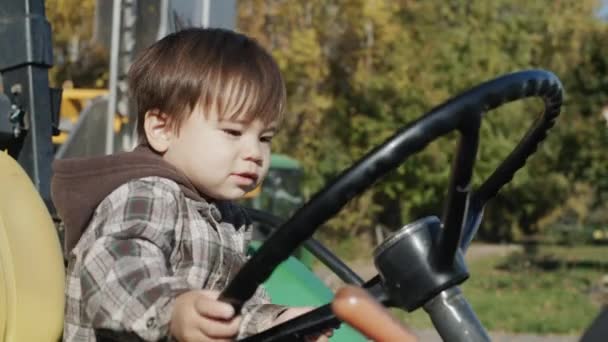 トラクターの運転手をしているアジアの子供はトラクターの車輪の後ろに座って. — ストック動画