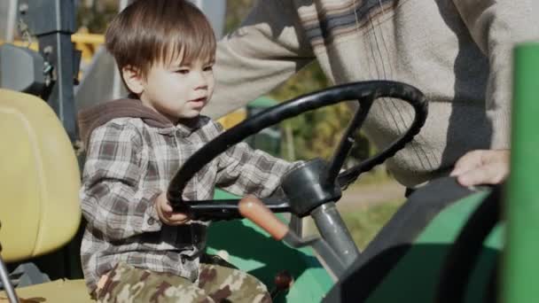 Um fazendeiro mostra a seu filho um trator, uma criança brincando ao volante — Vídeo de Stock