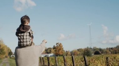 Bir çiftçi babası, küçük oğluna çiftliğe yerleştirilmiş rüzgar türbinini gösterir..