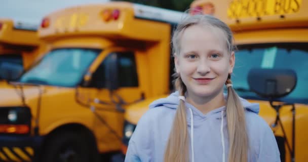 Retrato de una colegiala alegre sobre el fondo de una fila de autobuses escolares amarillos — Vídeos de Stock