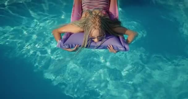 Vista superior: Un niño con coletas afro nada sobre un colchón inflable en la piscina, descansando y disfrutando del resto. — Vídeos de Stock