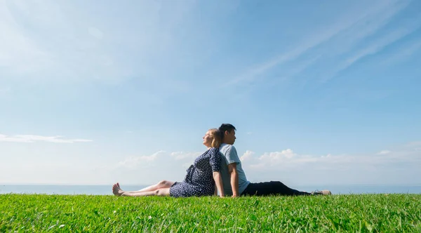 Ασιάτης άνδρας με μια έγκυο γυναίκα αναπαύονται στη φύση σε ένα γραφικό μέρος, κάθονται στο πράσινο γρασίδι — Φωτογραφία Αρχείου