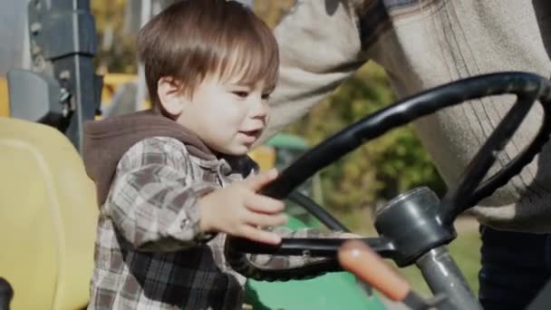 Bayi petani bermain di belakang roda traktor, di samping ayahnya — Stok Video